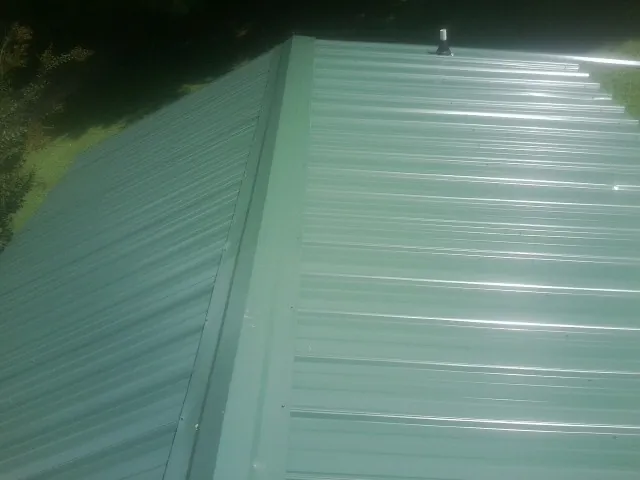 New green metal panels meeting at the ridge of a roof — Flat Roof Repair work by our crew in Towanda